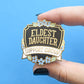 Eldest Daughter Support Group enamel pin black shield with blue flowers